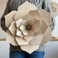 Large beige wooden flower held by a person wearing a gray sweater.
