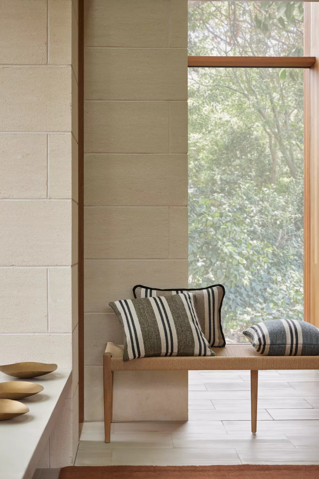 Wooden bench with striped cushions against a tiled wall and window view