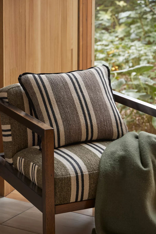 Chair with striped cushion and wooden frame in a room with a window showing greenery outside.