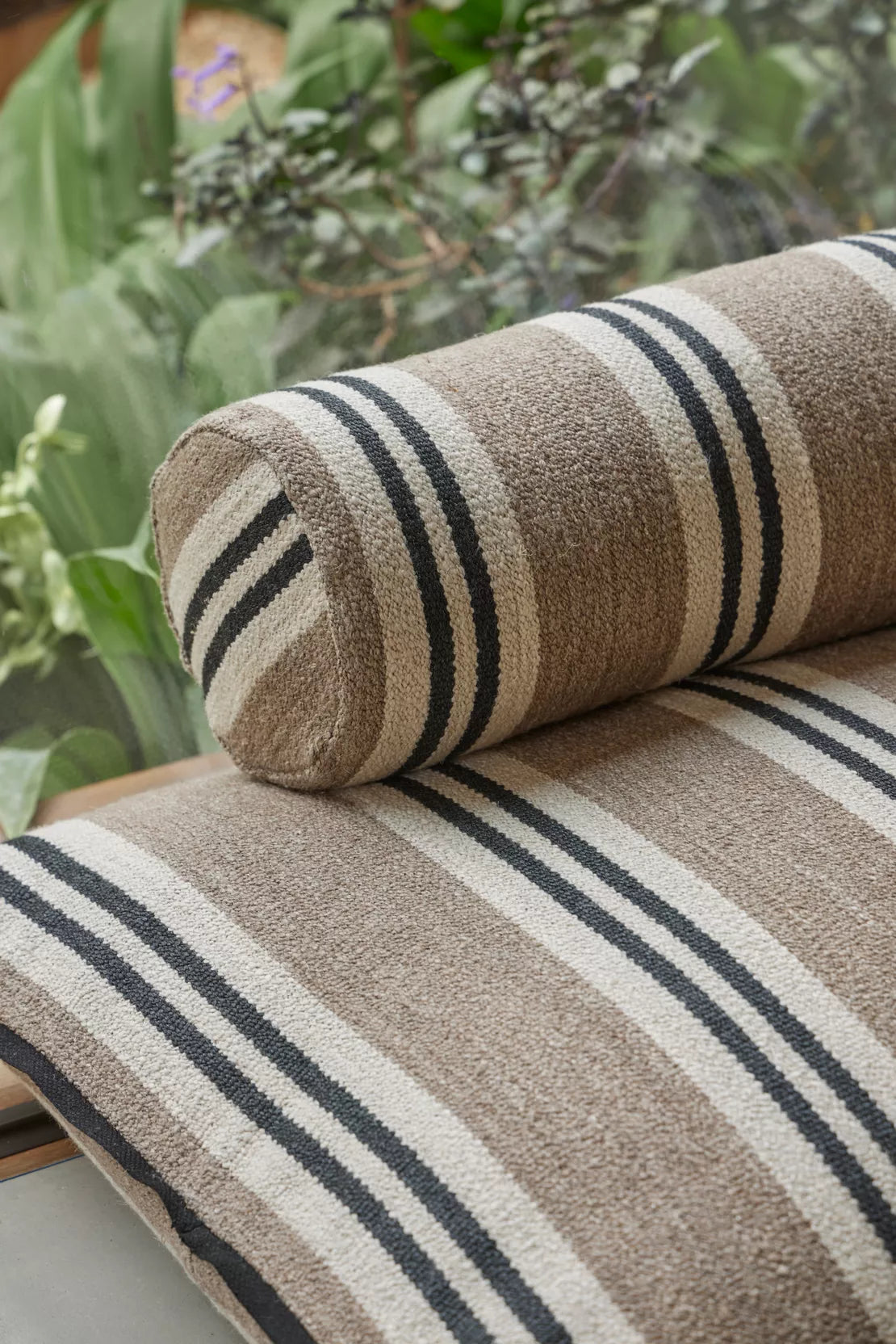 Striped fabric roll on a striped fabric surface with greenery in the background