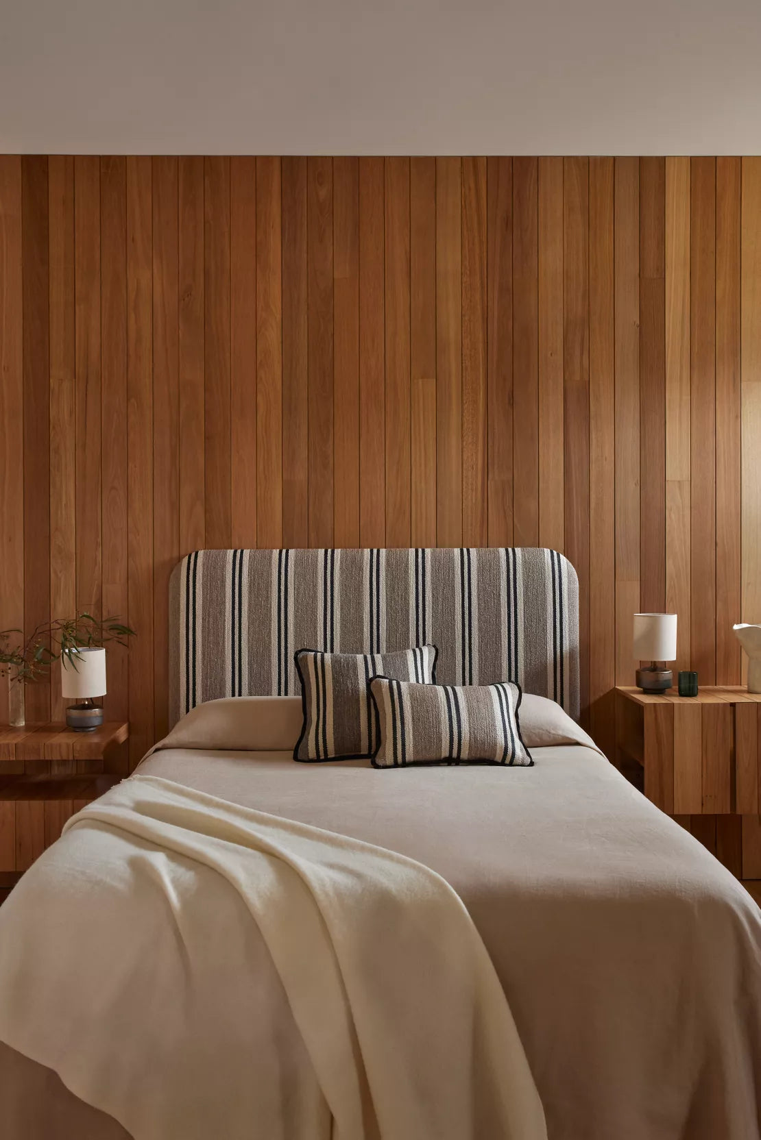 Bedroom with wooden wall paneling, striped headboard, and beige bedding.