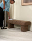 Person placing a book on a brown textured bench against a white wall.