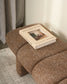 Brown textured ottoman with a book titled 'Curated Style' on top, against a neutral background.