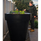 Person standing next to a large black planter with plants on a rooftop garden.