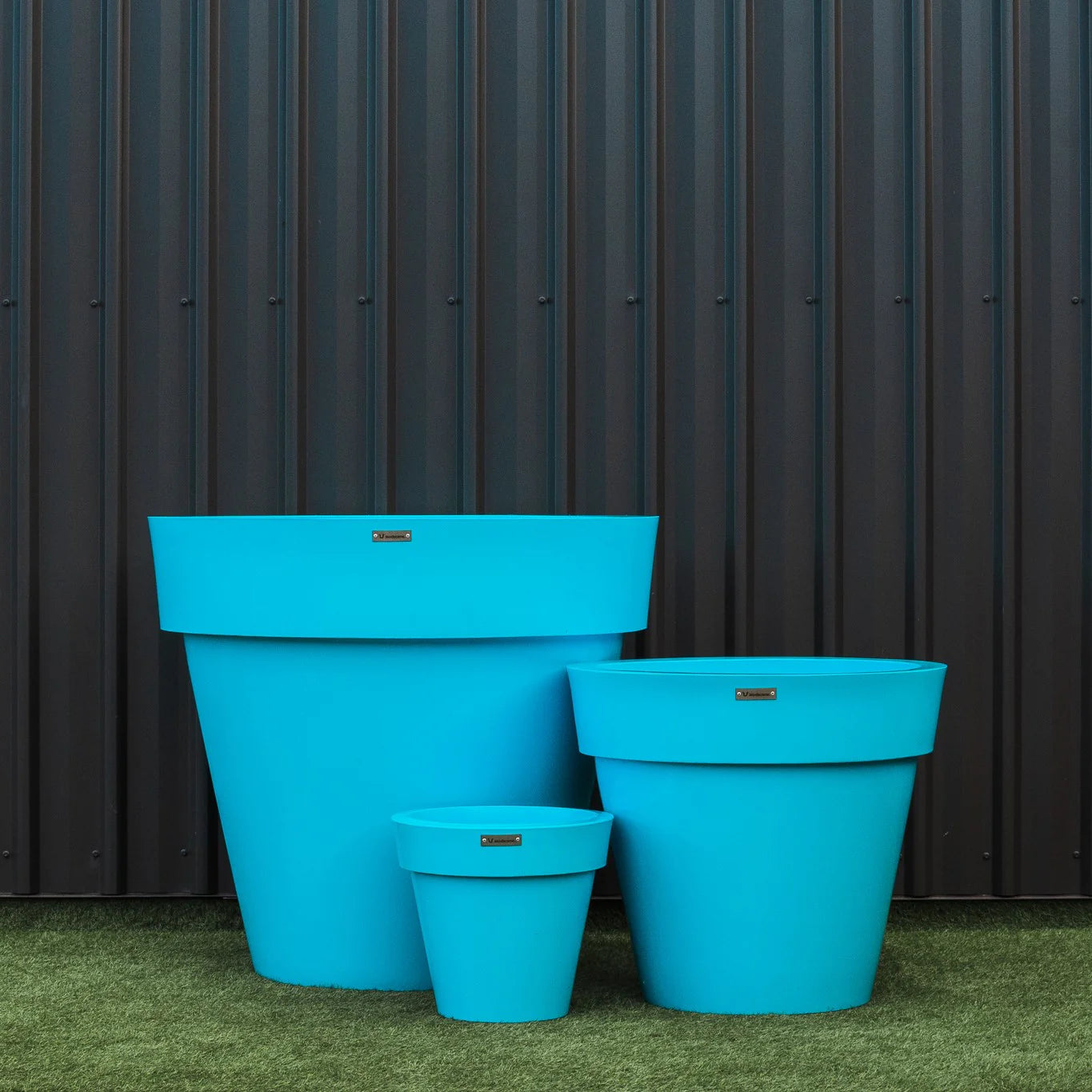 Three blue planters of different sizes against a dark metal wall.