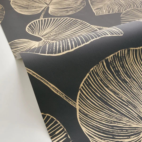 Black wallpaper with a gold botanical leaf pattern, shown partially unrolled over a white surface.