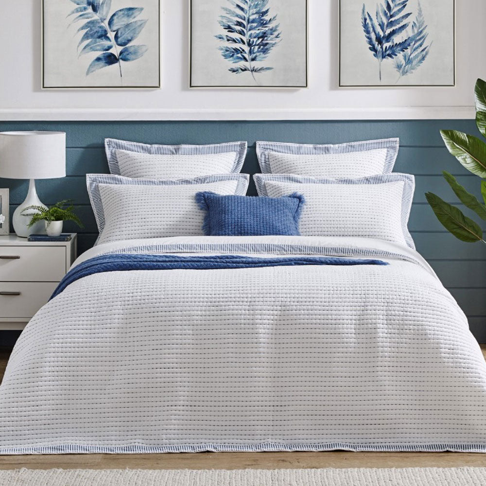 Marissa Coverlet and Oxford pillowcases in a bedroom setting with blue wooden slat walls with white wall above showing 3 paintings of blue and white leaf patterns