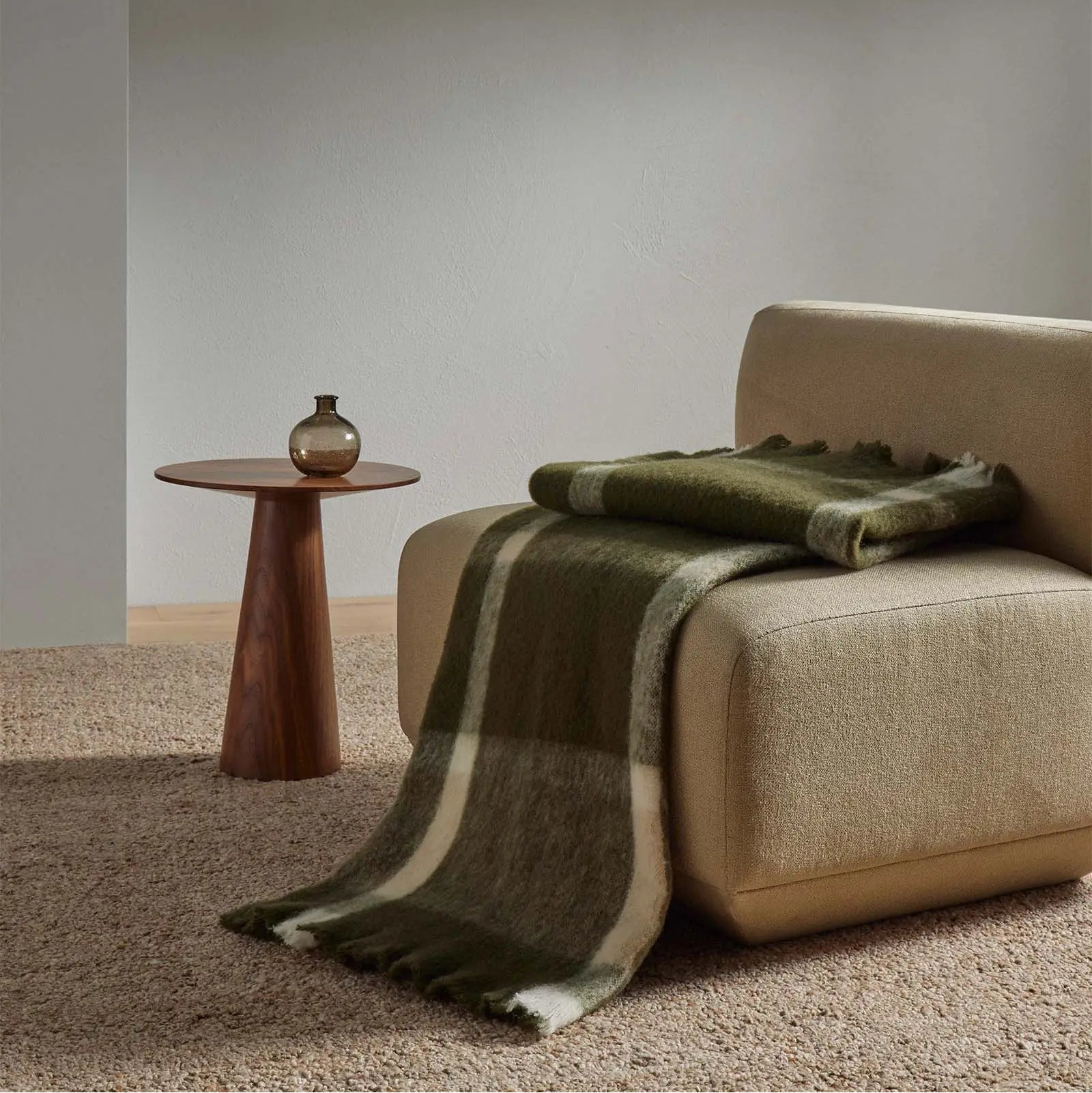 Checked Mayfield throw in olive and cream draped over a beige sofa chair with a small wooden side table and vase