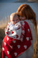 baby wrapped in a red and white hear merino blanket being held by a red haired lady, lake in background