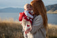 baby wrapped in a red and white hearts merino blanket being held by a red haired lady, lake and mountains in the background