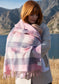 Mother with red hair holding a new born wrapped in a pink and white checked merino blanket with lake and mountains in background
