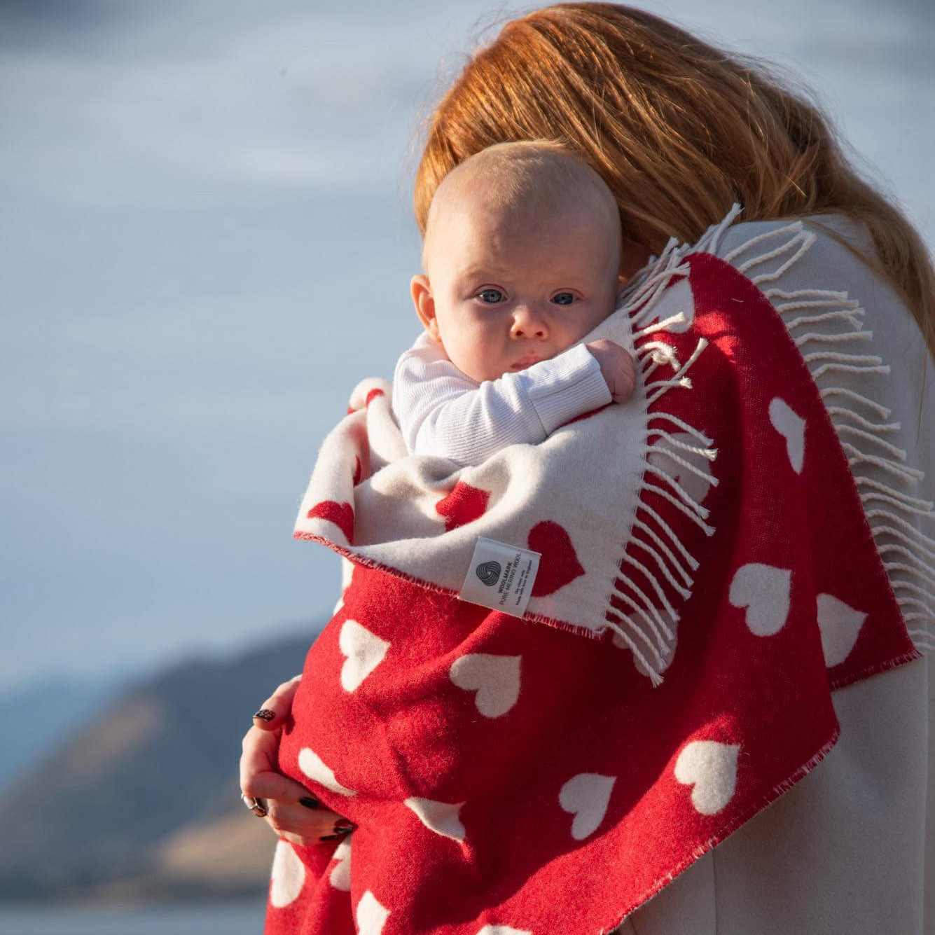 baby wrapped in a red and white hear merino blanket being held by a red haired lady