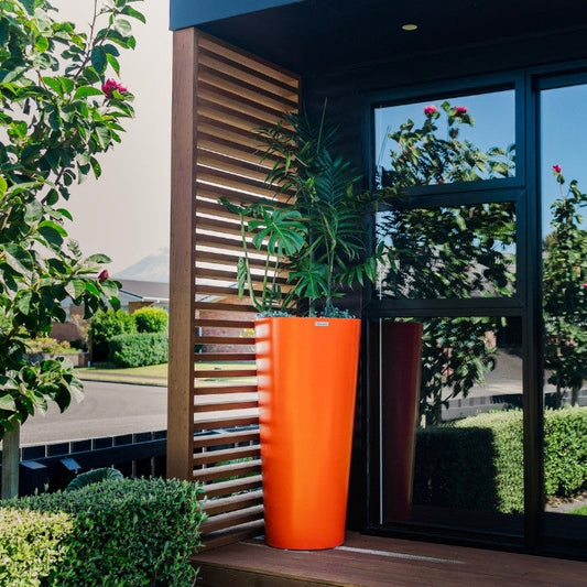 Orange planter with a plant in front of a glass door with a view of a garden.