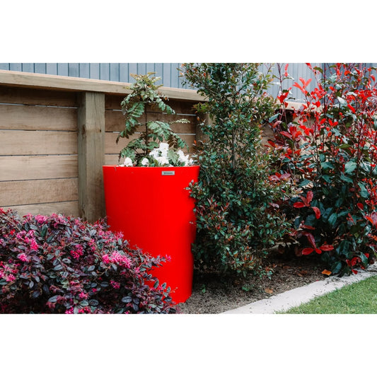 Red planter with plants against a wooden fence and garden backdrop