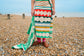 Person standing on a pebbly beach wearing a colorful patterned towel.
