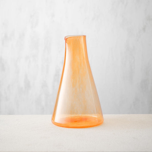 Monmouth glass carafe in orange, wide circular base with slim top for pouring. Glass is clear with orange streaks through it