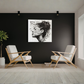 A black and white square wall art print featuring a stylized portrait with the text 'Borromeo Reno' is displayed on a dark wall in a modern living room setting with two white chairs and light wood flooring.