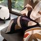 Decorative pillows with geometric patterns on a chair in a room with a window and lamp.