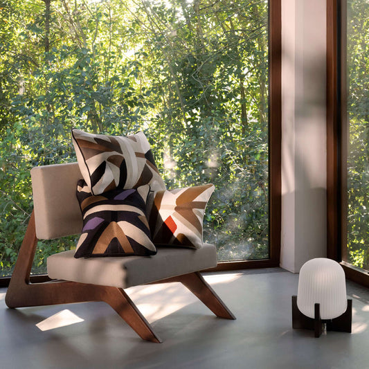 Modern chair with a patterned cushion in a room with large windows showing greenery outside.