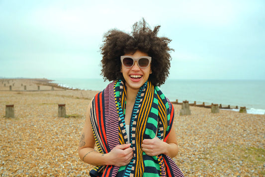 Woman with an afro wearing sunglasses and a colorful towel on a beach.