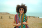 Woman with an afro wearing sunglasses and a colorful towel on a beach.