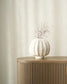 White textured vase with branches on a wooden side table against a beige wall