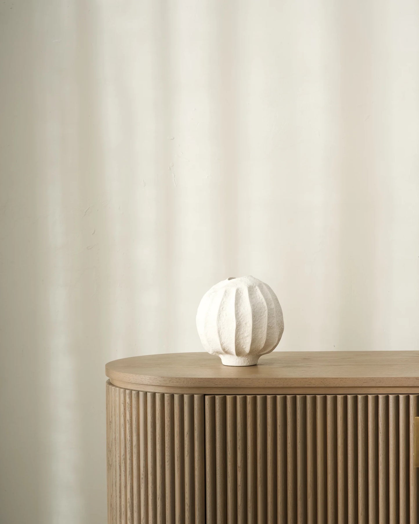 White ceramic vase on a wooden side table against a beige wall