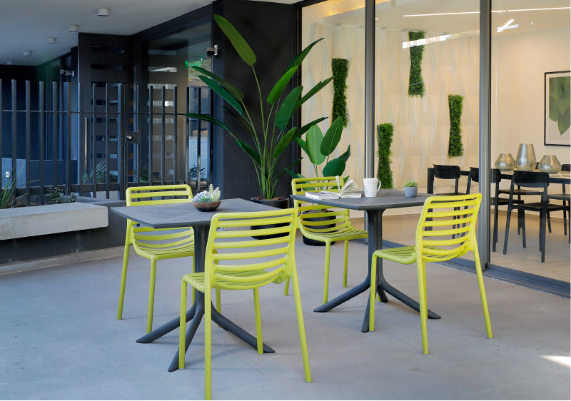 Modern outdoor seating area with green chairs and tables in a building setting.