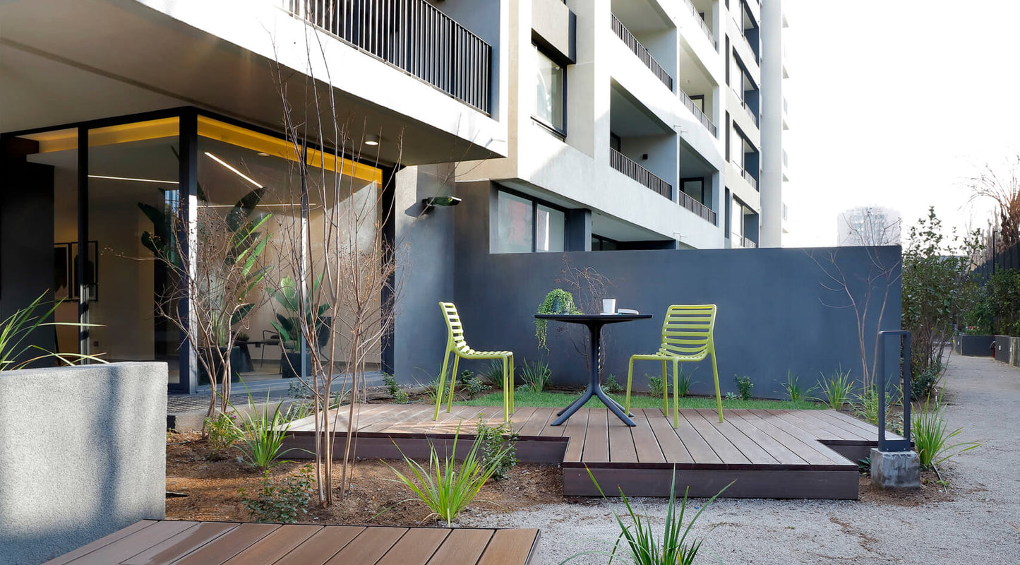 Modern outdoor seating area with green chairs and a small table in an urban setting.