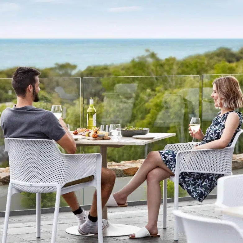 Couple sitting at a table on a balcony with a scenic view of trees and water.