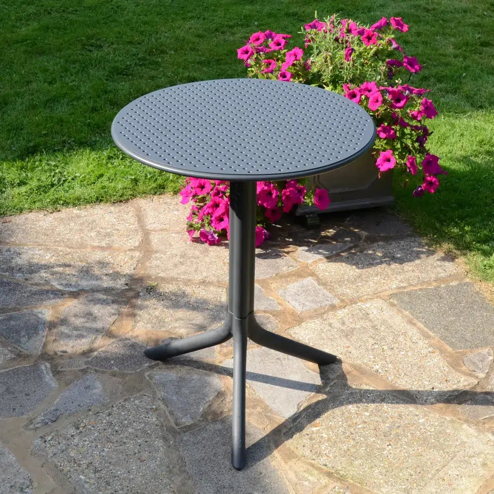 Round black outdoor table on a stone patio with pink flowers in the background