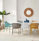 A dining table set with six modern mesh chairs in assorted colors including teal, gray, white, yellow, and brown, styled in a bright minimalist dining room with a round wooden wall mirror.