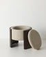 A modern cylindrical stool with a dark brown wooden frame and a textured beige bouclé seat, shown with its matching oval backrest leaning against it on a white studio background.
