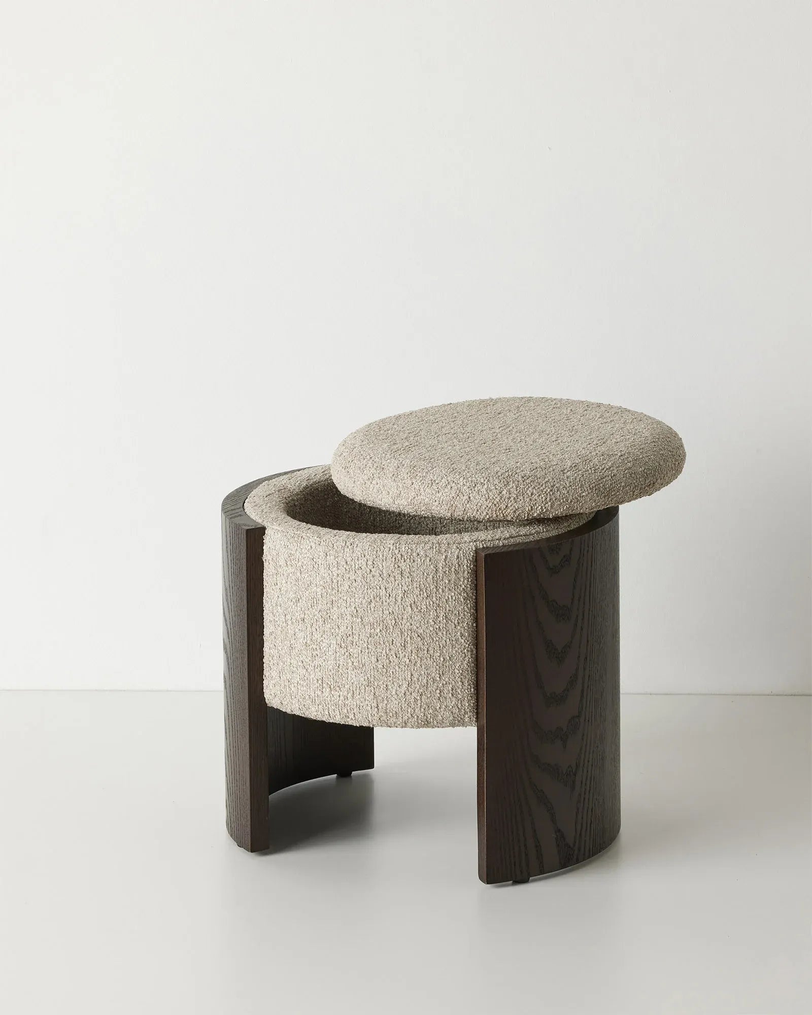A modern round ottoman stool with a textured beige bouclé fabric seat and a dark brown wood frame, shown on a clean white studio background.