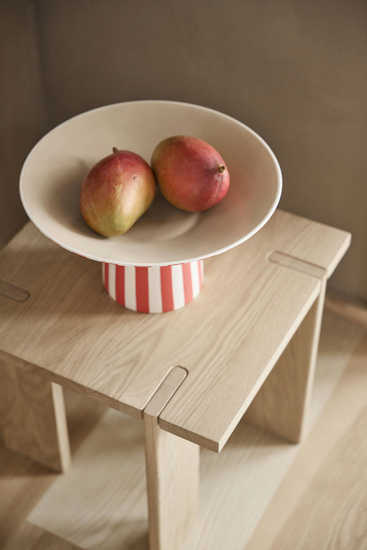 Bowl with mangoes on a wooden stool against a neutral background