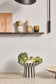 Striped ceramic bowl with vegetables on a wooden surface, with a shelf and decor items in the background.