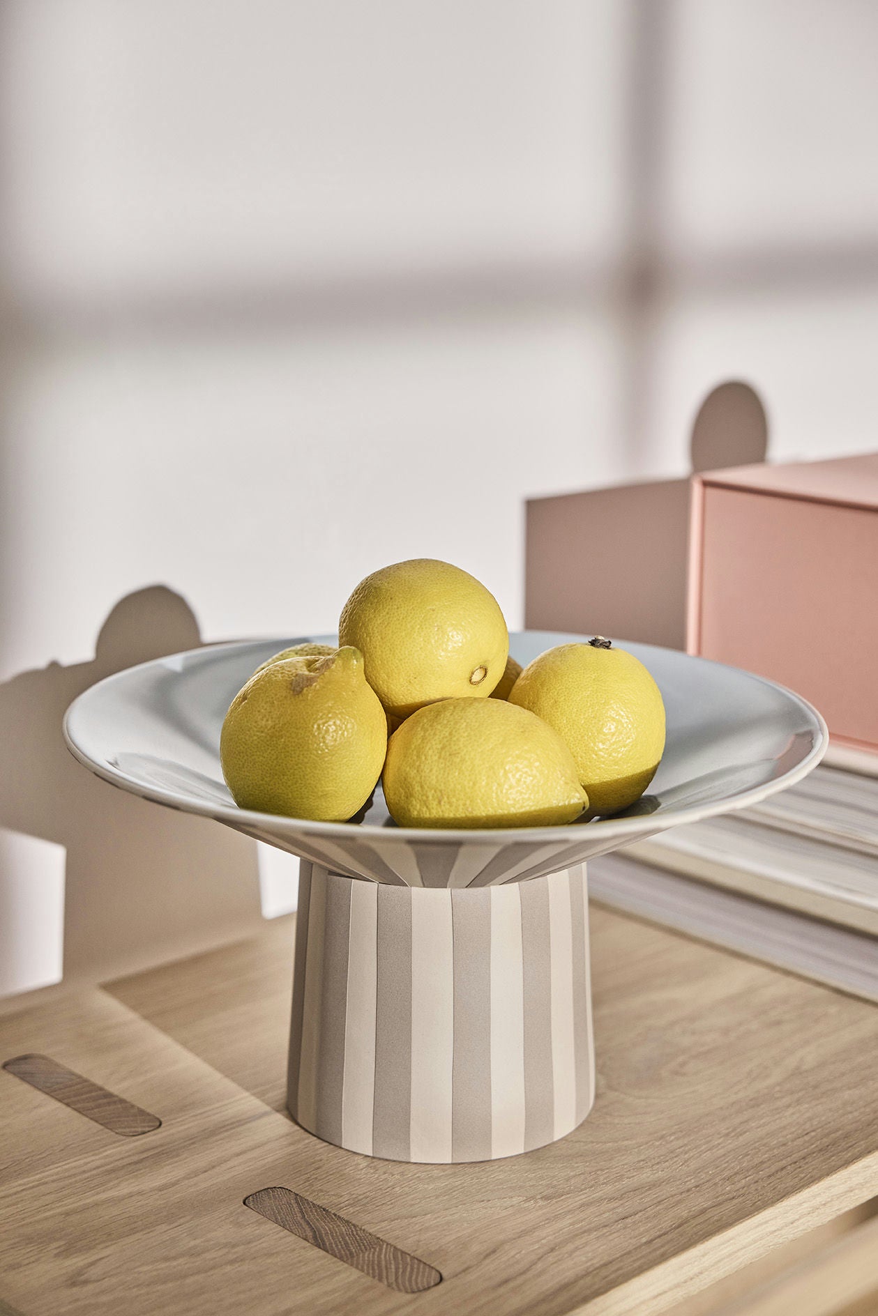 Striped ceramic pedestal with lemons on a wooden surface