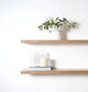 Two oak floating shelfs wiht a plant and candle on against a white background