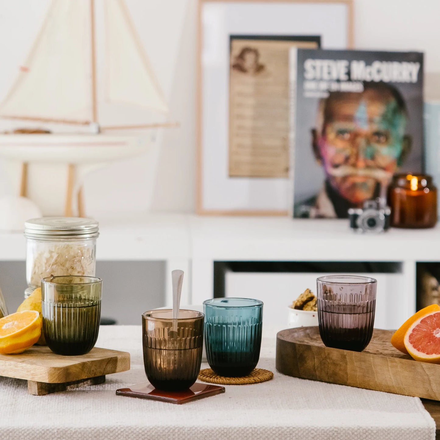 Colorful glass tumblers on a table with a magazine and decor items in the background.