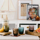 Colorful glass tumblers on a table with a magazine and decor items in the background.