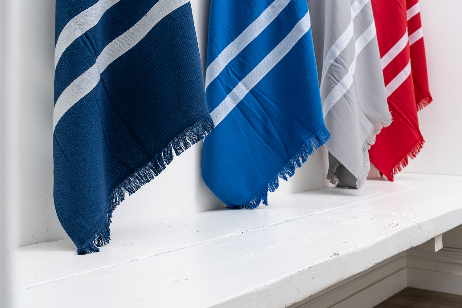 Four striped towels in blue, white, gray, and red hanging on a white shelf.