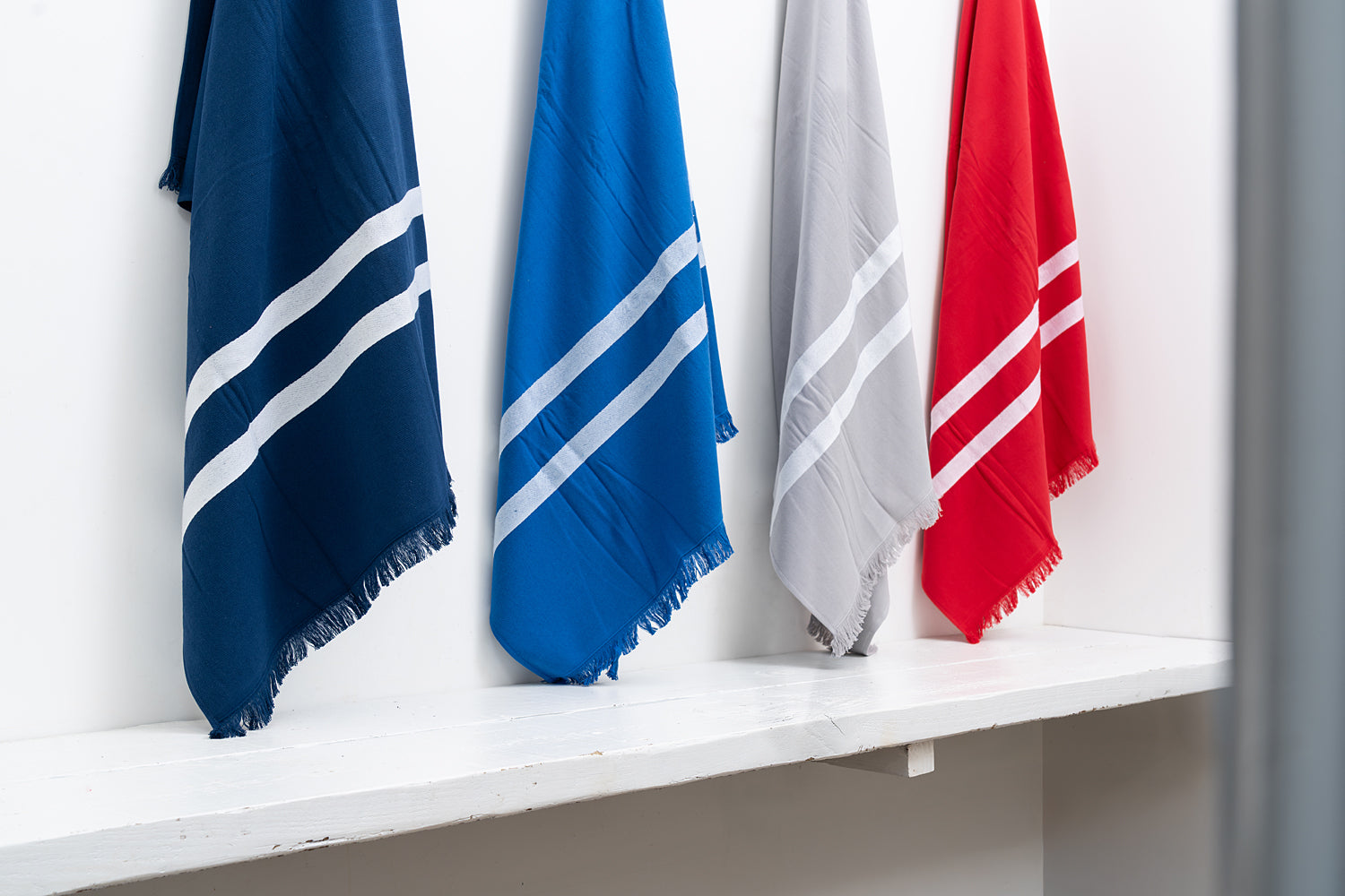 Four scarves in blue, red, and gray with white stripes on a white shelf.