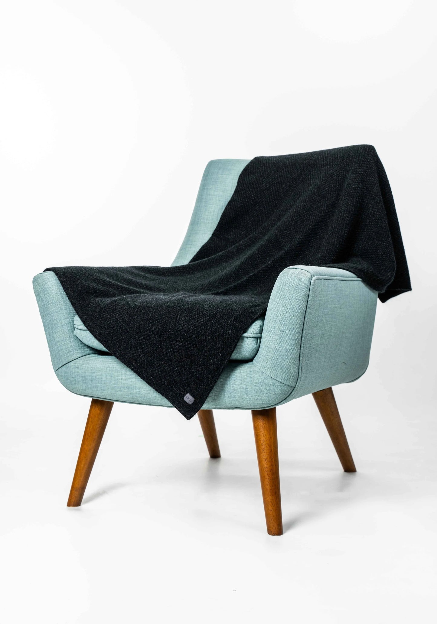 A light blue upholstered armchair with wooden legs, draped with a dark charcoal knit throw blanket, photographed on a clean white studio background.
