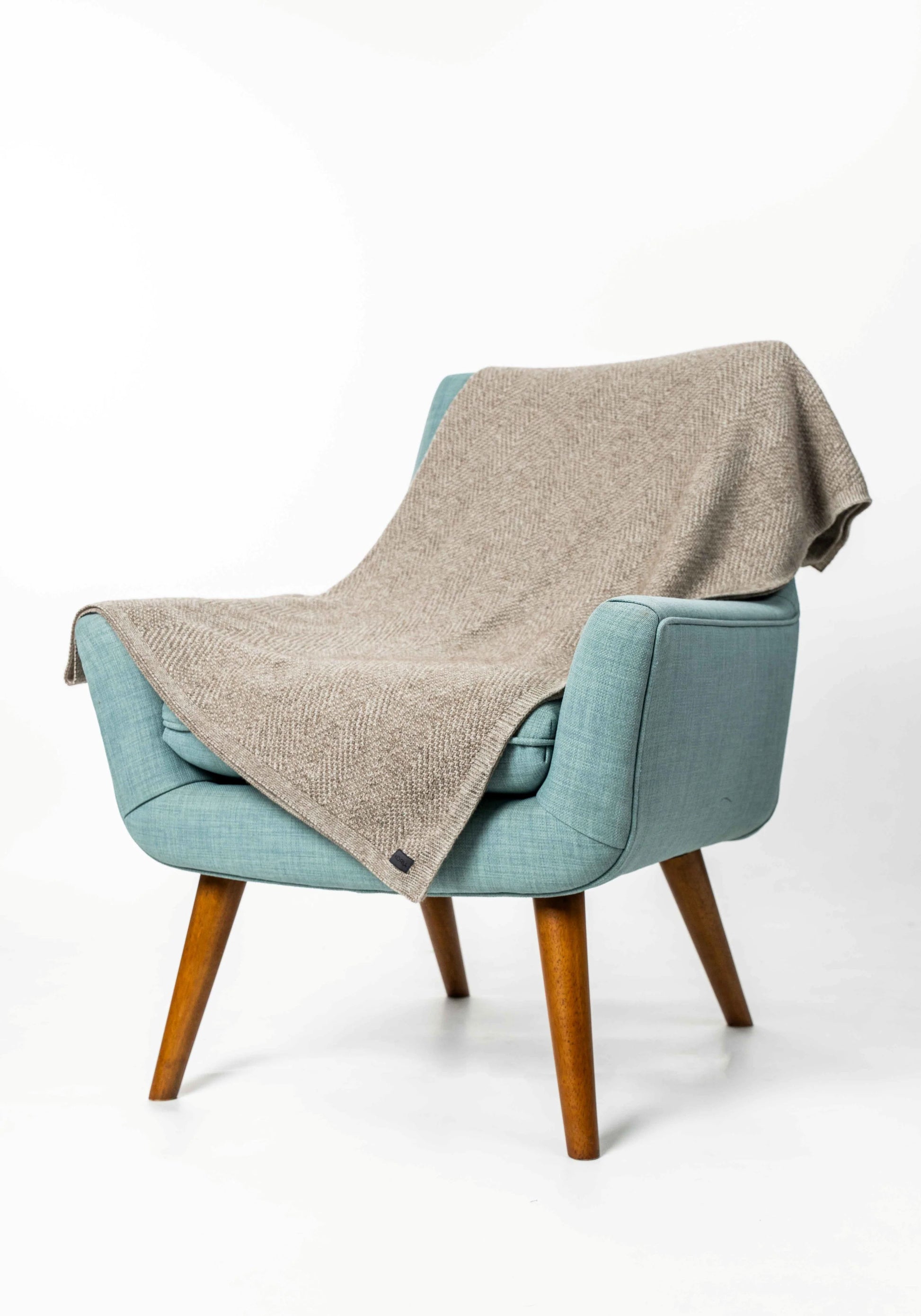 A light blue upholstered armchair with wooden legs, draped with a textured beige throw blanket, photographed against a clean white studio background.