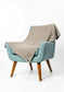 A light blue upholstered armchair with wooden legs, draped with a textured beige throw blanket, photographed against a clean white studio background.
