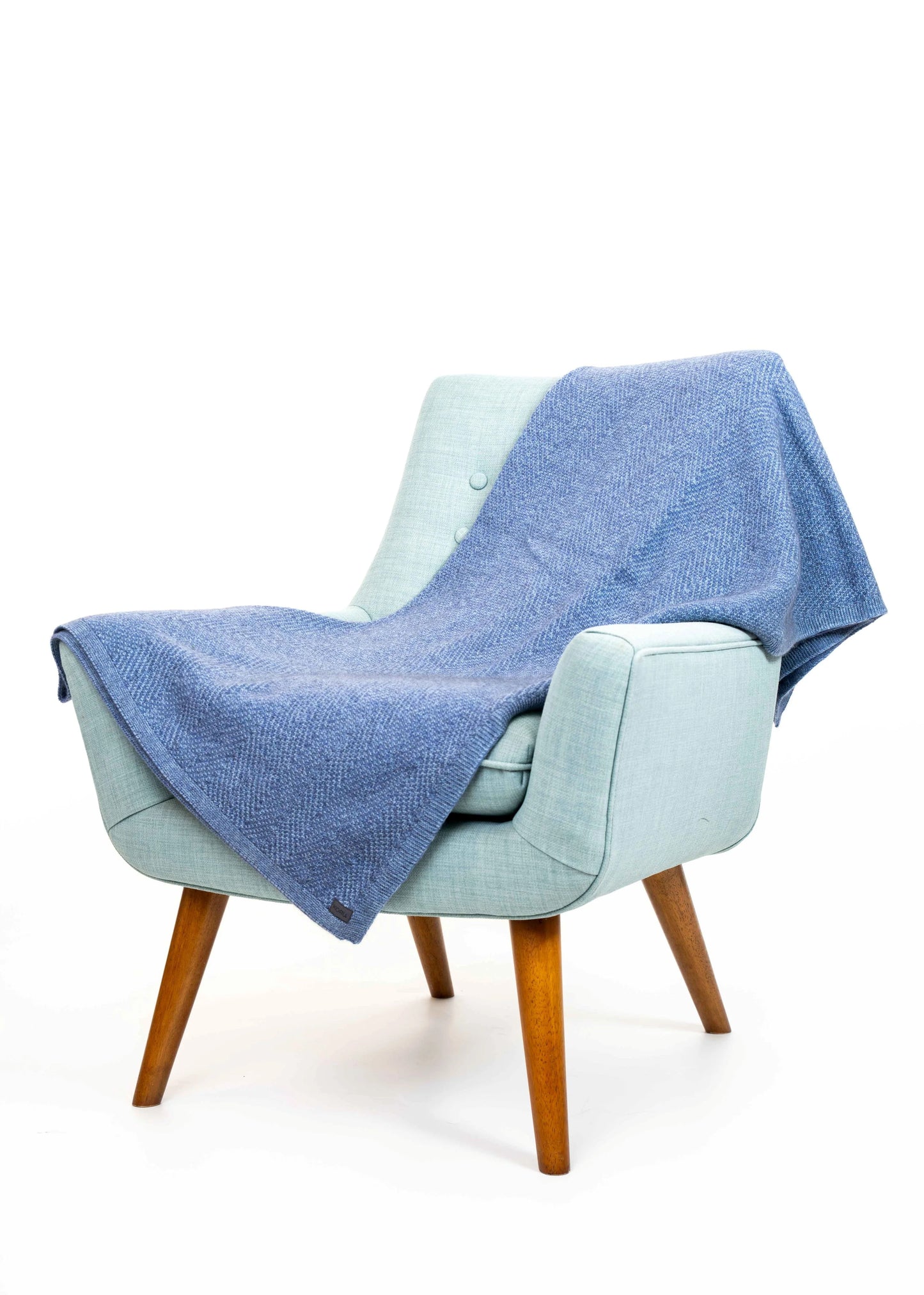 Light blue armchair with a blue blanket draped over it on a white background