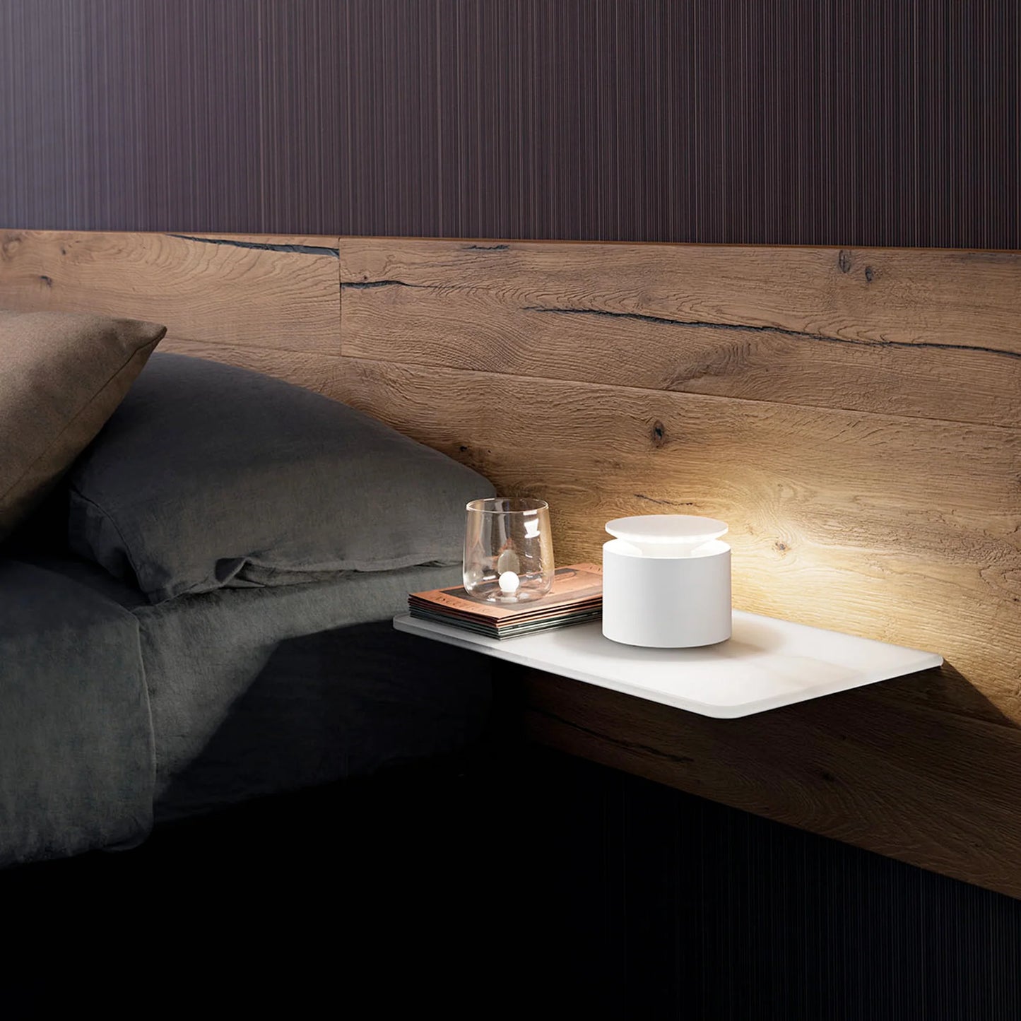 Small nightstand with a lamp and glass against a wooden headboard