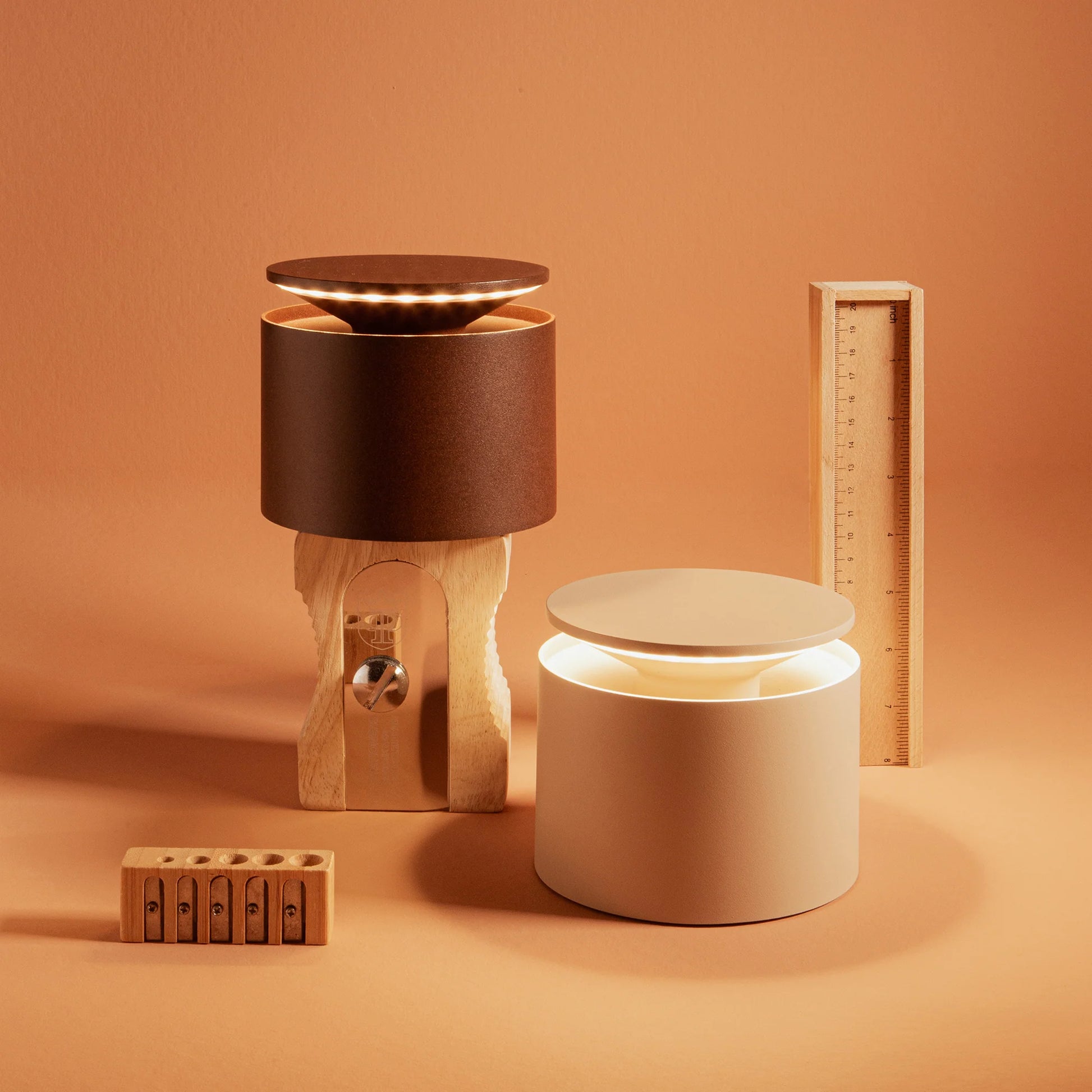 Two cylindrical lamps, one brown and one beige, on an orange background with wooden objects.