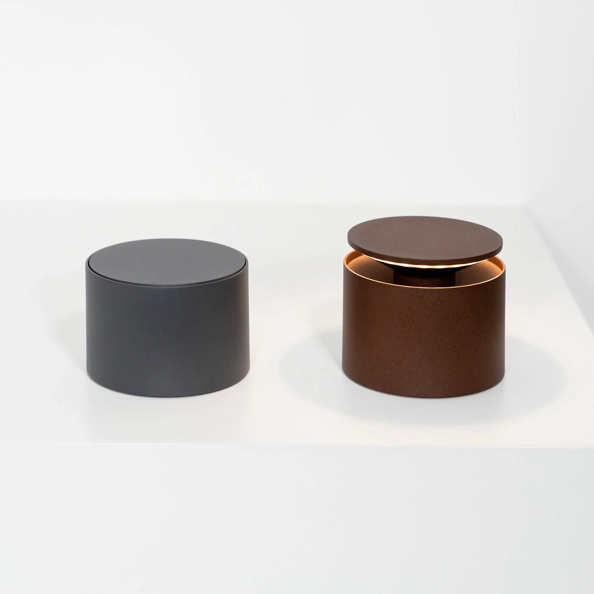 Two cylindrical lights, one black and one brown with a gold interior, on a white background.