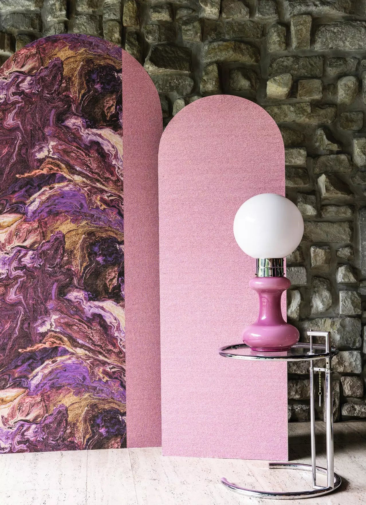 Pink lamp with white bulb on a small round table against a textured wall.